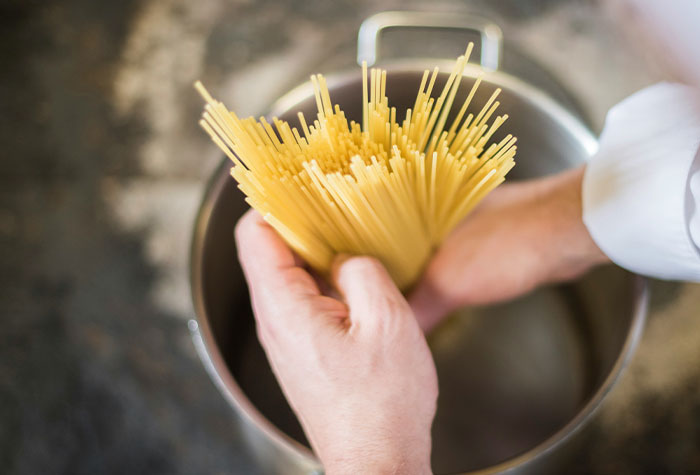 Hands holding uncooked spaghetti over a pot, illustrating common cooking advice in kitchen food preparation.