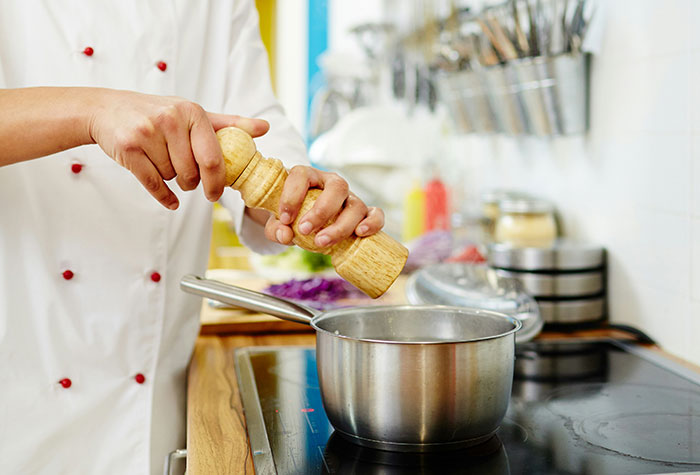 Chef seasoning food in a pot on stovetop illustrating common cooking advice that often doesn't improve dishes.