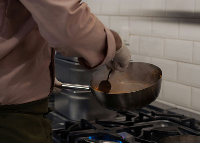 Person stirring steaming food in a pan on a gas stove cooking in a kitchen following common cooking advice.