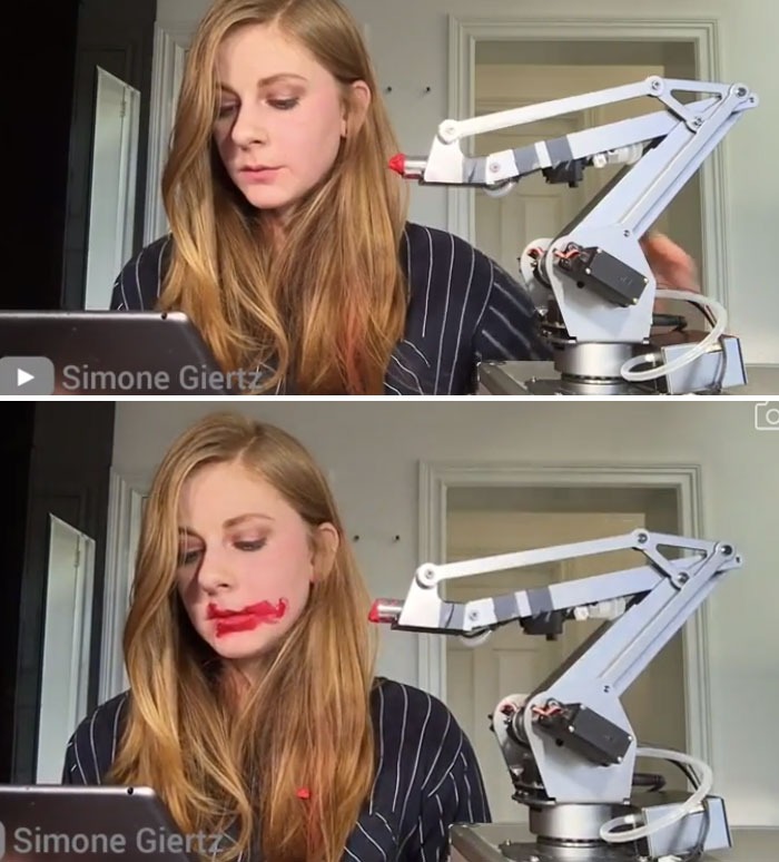 Woman with long hair using a robotic arm that hilariously fails, smearing red paint on her face as a tech fail moment.