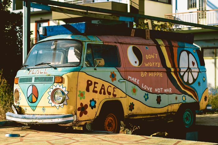 Old hippie van with peace signs and colorful flower designs parked in a forgotten tourist destination worldwide.