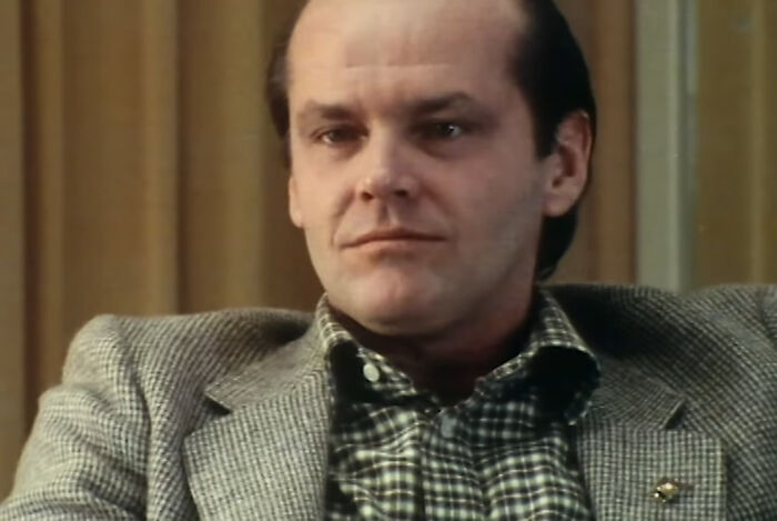 Man in a checkered shirt and grey blazer sitting indoors, reflecting the spirit of bartenders sharing wild tales behind the tap.