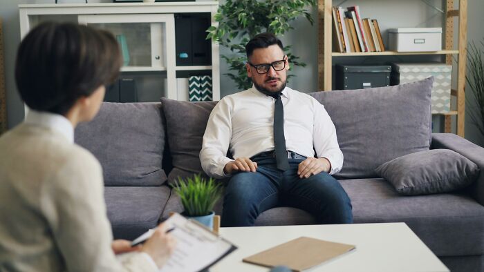 Man in white shirt and tie sitting on couch during a conversation about strange and dumb things heard from recruiters.