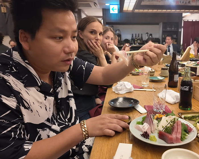 Vlogger sitting at a restaurant table with sushi, recording a video unaware of the A-list star nearby.