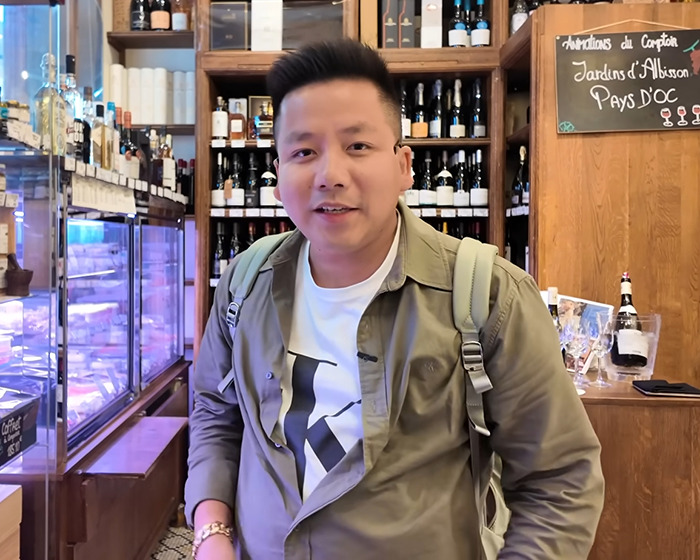 Vlogger wearing backpack inside a store, recording video unaware of sitting next to an A-list star among wine bottles.
