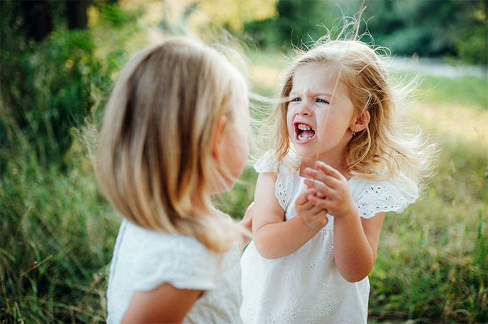 Two young girls in white dresses outdoors, one visibly upset, representing a woman storming out after engagement dinner drama. Two young girls in white dresses outdoors, one visibly upset, representing a woman storming out after engagement dinner drama.
