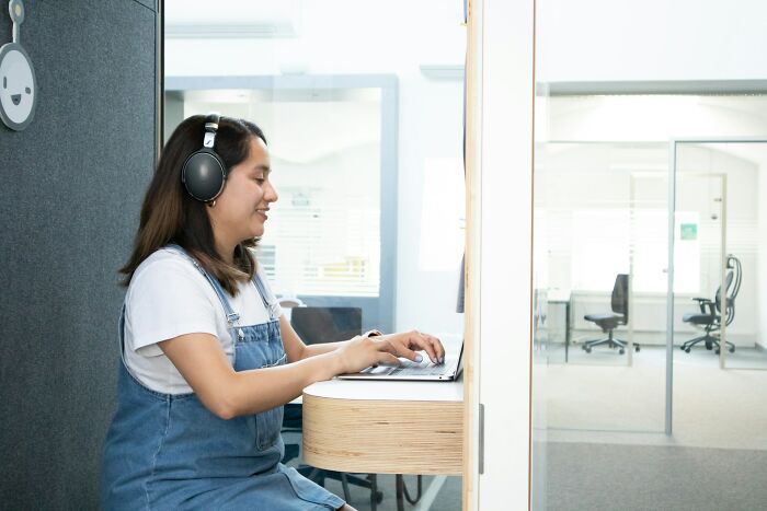 Woman wearing headphones working on laptop in small office booth, illustrating jobs and earning perceptions online.