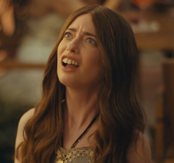Aimee Lou Wood with long brown hair, looking surprised and concerned in a dimly lit indoor setting.