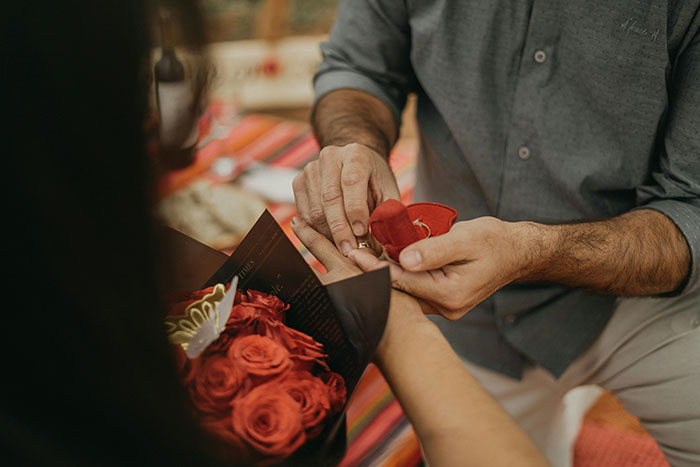 Man proposing with engagement ring to woman holding red roses, symbolizing sister&rsquo;s fianc&eacute; and wedding conflict scenario.
