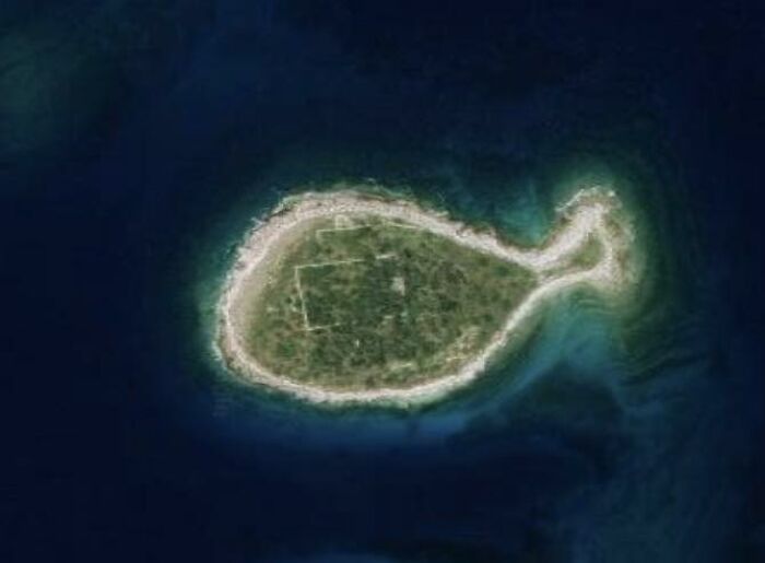 Aerial view of a small, oddly shaped island surrounded by blue water, found on Google Earth.