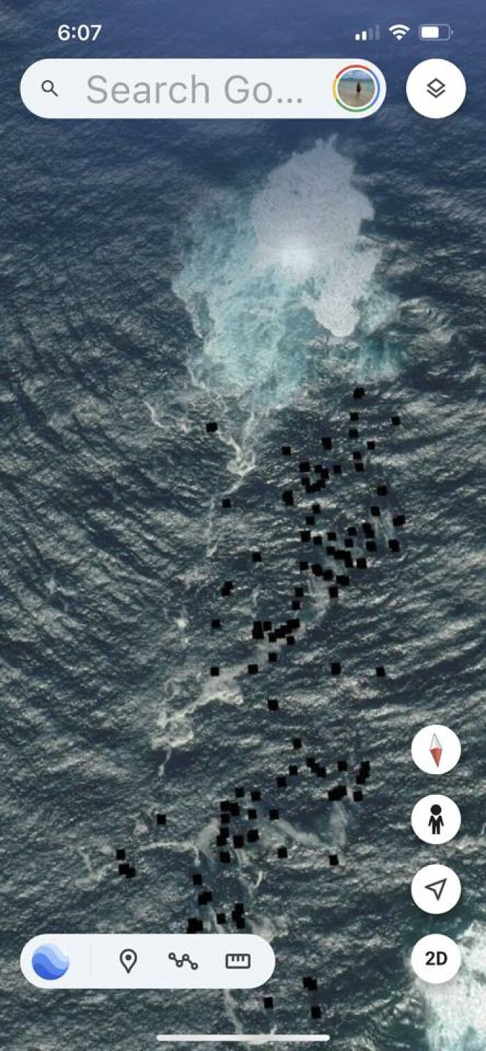 Satellite view of an ocean area on Google Earth showing unusual black pixelated spots in the water surface.