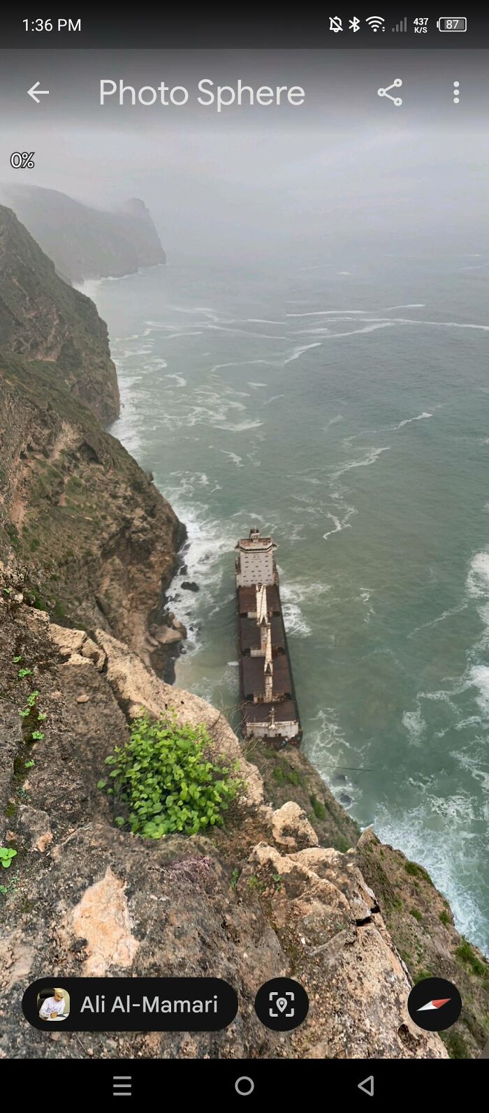 Aerial view of a rusted shipwreck along rocky cliffs and rough sea, an odd discovery on Google Earth.