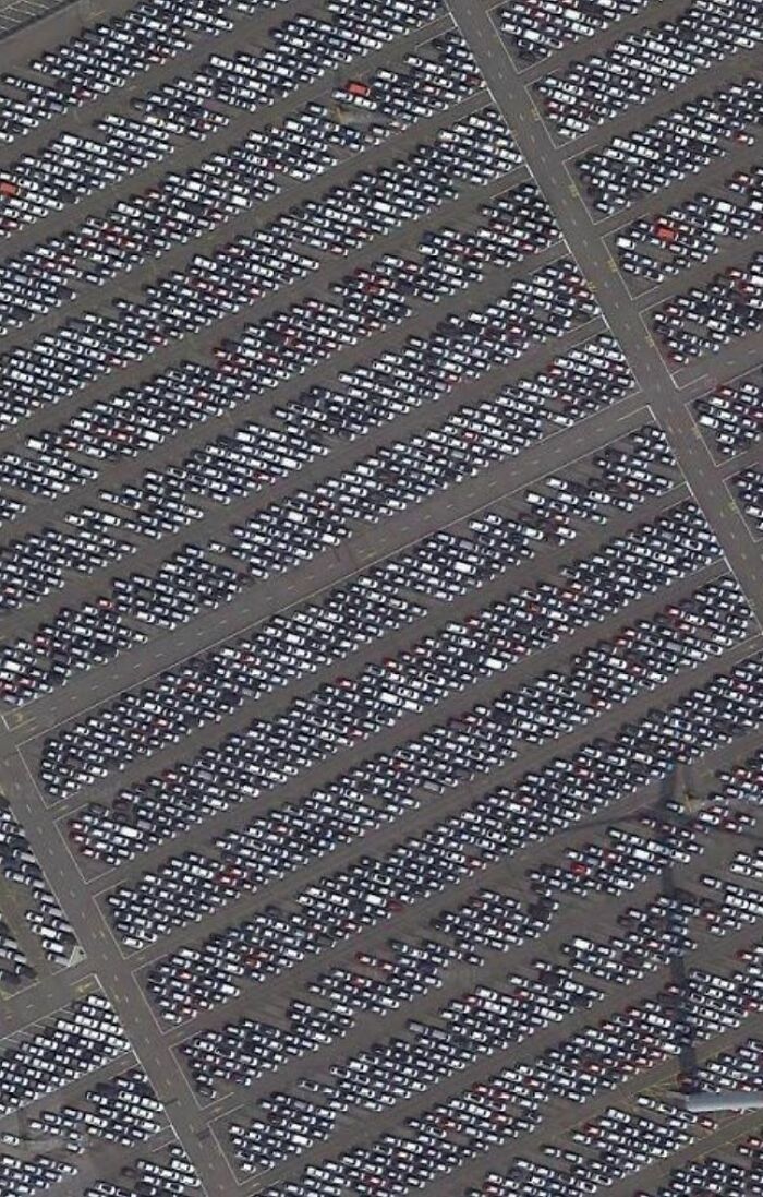 Aerial view of an enormous parking lot filled with thousands of neatly lined cars, featuring odd patterns on Google Earth.