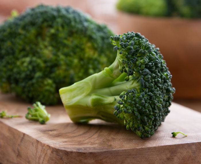 Fresh broccoli on a wooden cutting board, representing healthy food that can help burn fat better with Ozempic.