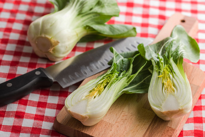 Fresh bok choy cut on a wooden board next to a knife on a red and white checkered tablecloth representing food that burns fat better with Ozempic