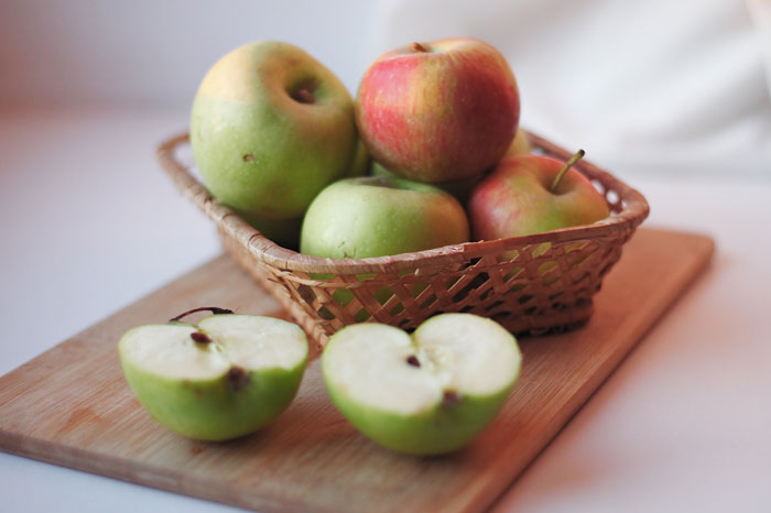 Basket of fresh apples and green apple halves on a wooden board showing food that may burn fat better with Ozempic.