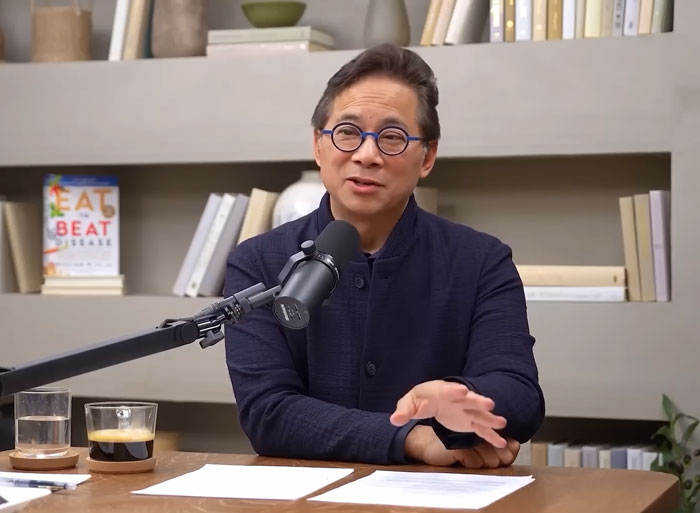 Man with glasses speaking into microphone, discussing what food burn fat better than Ozempic in a studio setting.