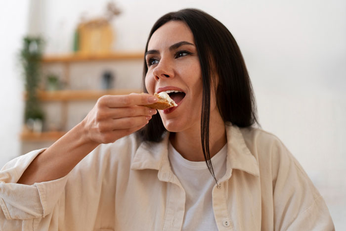 Woman eating toast with cream in a bright kitchen, focusing on what food burn fat better with Ozempic benefits