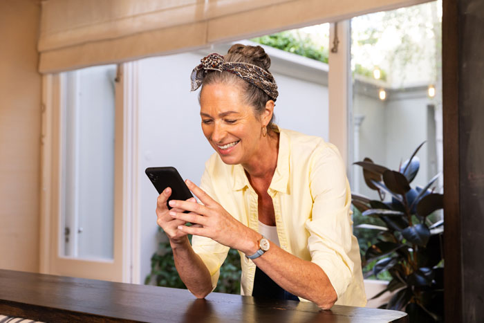 Woman smiling and texting on phone at kitchen counter during wife&rsquo;s catch-up with her ex turning into a sleepover scenario.