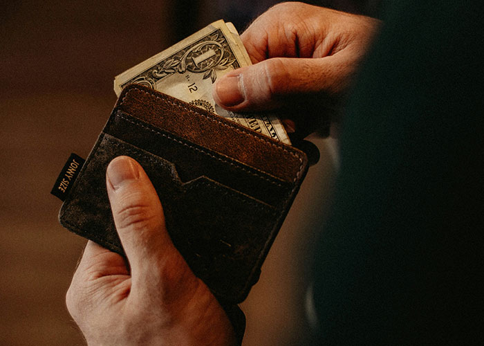 Man removing a dollar bill from a brown leather wallet, representing financial struggles after losing a job.