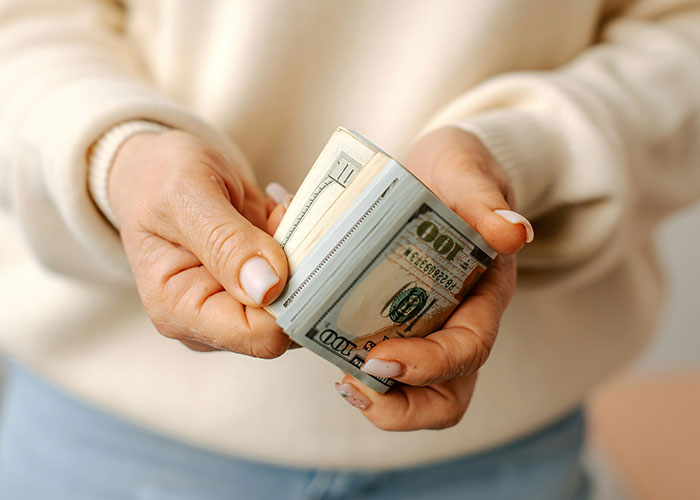 Hands holding a stack of hundred-dollar bills symbolizing refusal to support husband&rsquo;s mom after job loss.