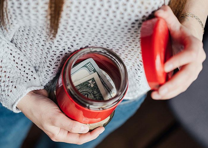 Person holding open jar with money inside, symbolizing refusal to support husband's mom after job loss.