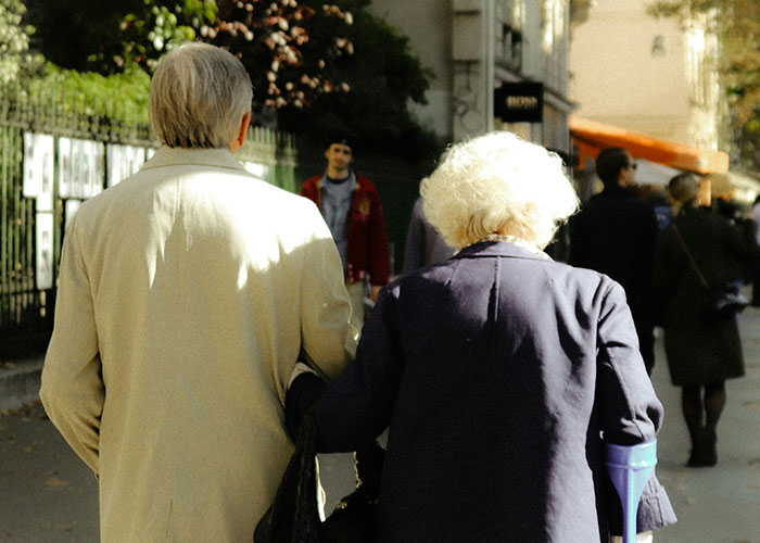 Elderly couple walking arm in arm on a sunny street, illustrating family support themes after job loss.