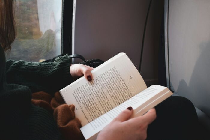 Person reading a book on a train holding a tiny thing that made the trip better during travel window view visible