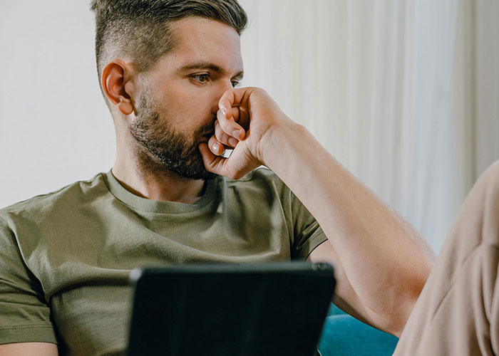 Man in green shirt looking thoughtful while holding his fist to his mouth, illustrating fake relationship and rejection.