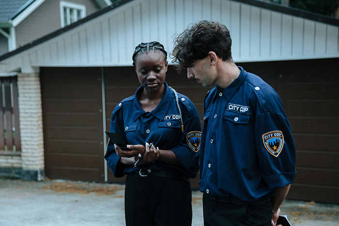 Two city cops in uniform outside a house discussing a case involving a man who called CPS about his sisters.