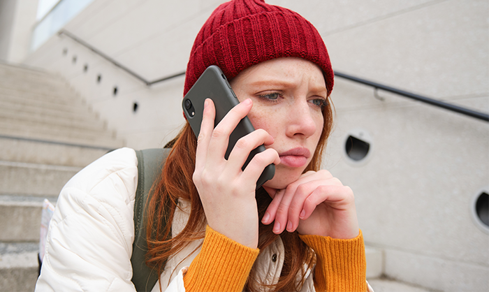 Young woman wearing a red beanie makes a serious phone call after discovering mom left little sisters at empty house.