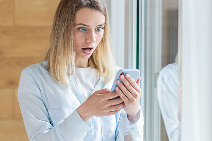Woman shocked while reading texts on smartphone, reflecting conflict from posting SIL's texts online and making her look bad