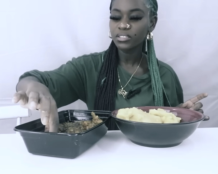 Woman with braided hair sitting at a table, dipping finger into food, related to animal torturing on camera topic.
