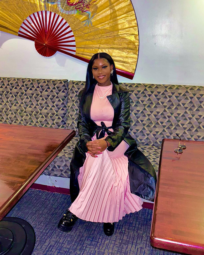 Young woman sitting indoors wearing a pink dress and black coat, linked to animal torture for social media likes.