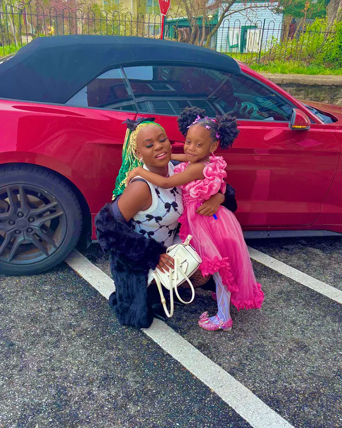 Woman with colorful hair and child in pink dress posing by a red car, unrelated to animal torture or prison time news.