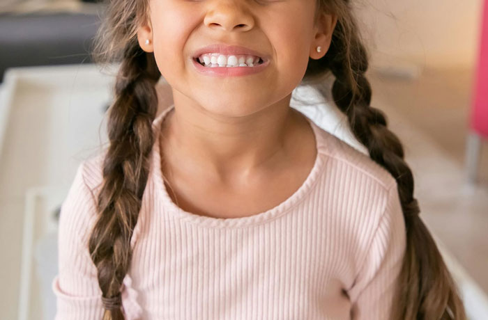 Young girl smiling with newly pierced ears, showing small earrings and braided hair indoors. Young girl smiling with newly pierced ears, showing small earrings and braided hair indoors.