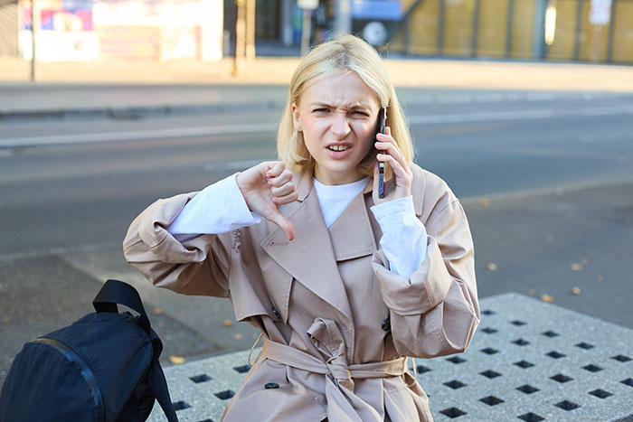 Woman on phone showing thumbs down gesture outdoors, illustrating con artist Karen stopped by Dunkin Donuts customer. Woman on phone showing thumbs down gesture outdoors, illustrating con artist Karen stopped by Dunkin Donuts customer.