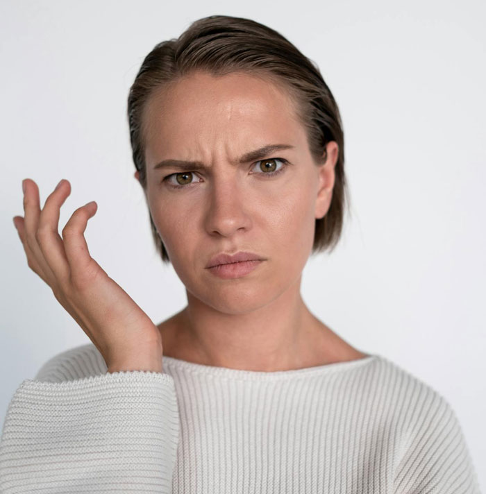 Confused woman in a white sweater raising her hand, reflecting on babysitter choice involving husband&rsquo;s ex.