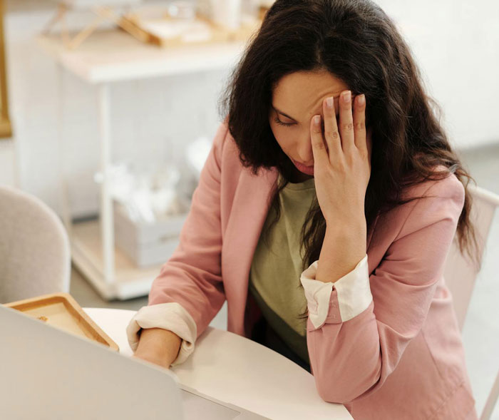 Woman looking stressed while sitting at a table using a laptop, considering babysitter options including husband&rsquo;s ex.
