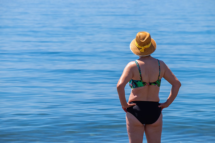 Woman in a swimsuit and sunhat standing by the water, evoking themes of betrayal and topless behavior in relationships. Woman in a swimsuit and sunhat standing by the water, evoking themes of betrayal and topless behavior in relationships.