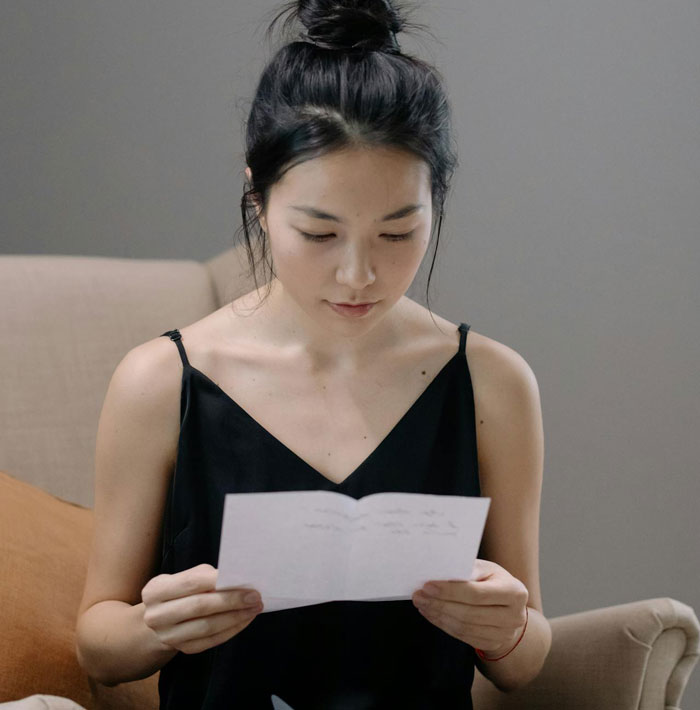 Woman reading a letter about fianc&eacute; attending friend's wedding without her, showing concern and contemplation indoors.