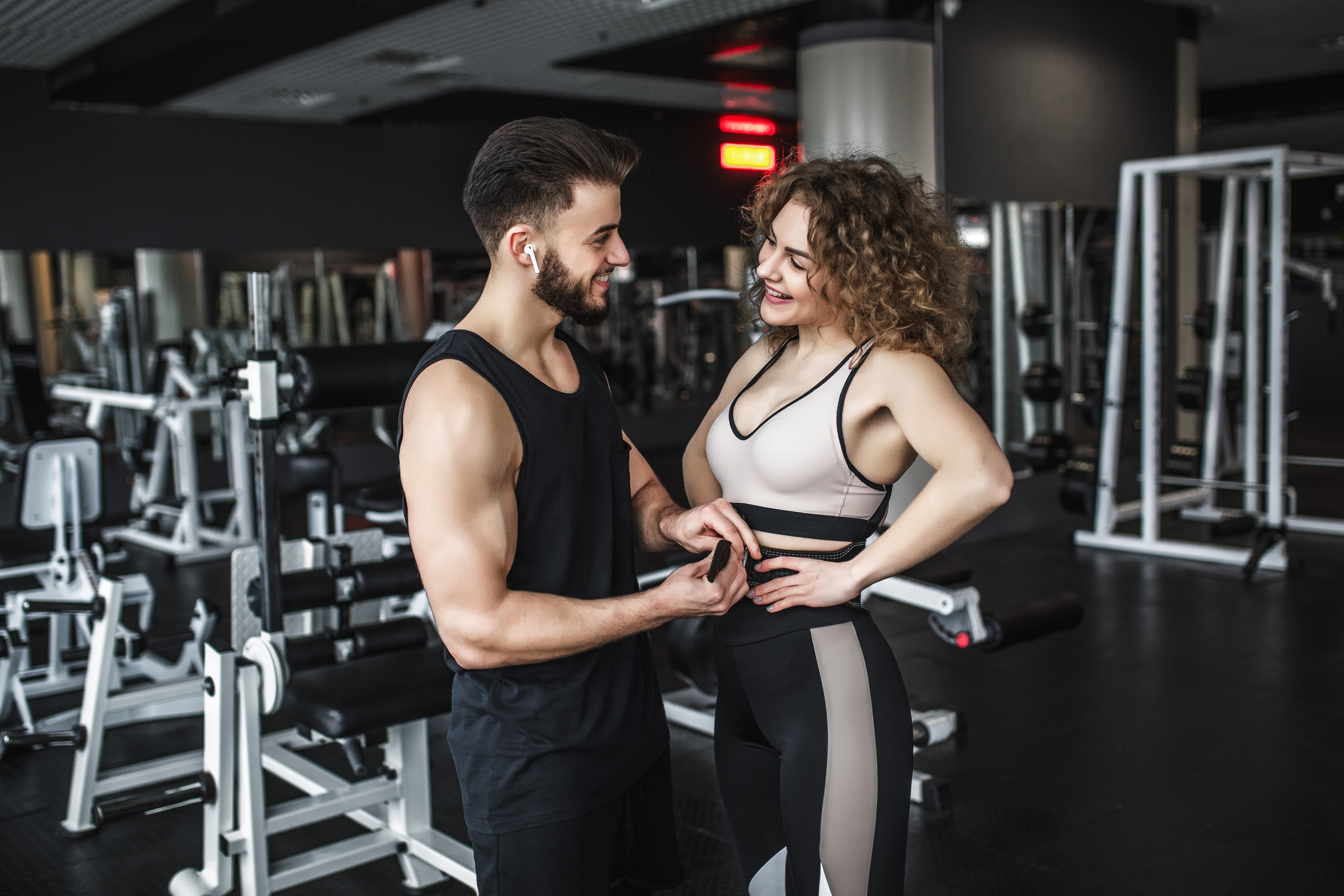 Young fit man and woman flirting at the gym, smiling and interacting among exercise machines and weights.