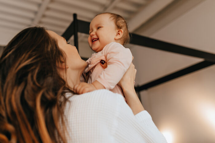 Mother holding and smiling at her happy baby indoors, capturing the joy of hilariously bad names and parenting moments.