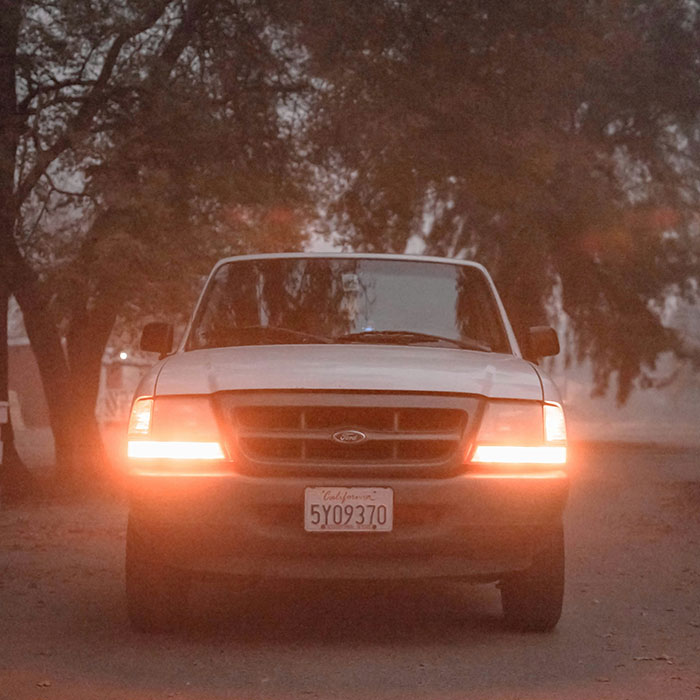 White truck with headlights on at dusk in a wooded area, illustrating unhinged safety habits shared by women.