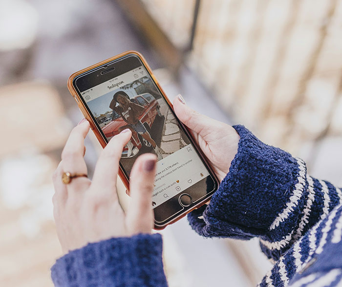 Person wearing a blue sweater scrolling through Instagram on a smartphone featuring shared safety habits by women.