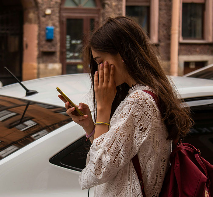 Young woman using phone outside by car, illustrating unhinged safety habits shared by women that might save lives