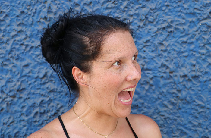Woman with dark hair in a bun showing an unhinged safety habit against a textured blue background.