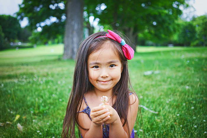 Young girl with a pink bow sitting on grass outdoors, symbolizing safety habits shared by women that might save lives