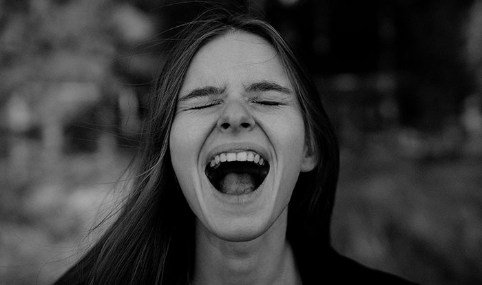 Young woman with long hair laughing outdoors, illustrating unhinged safety habits shared by women that might save lives.
