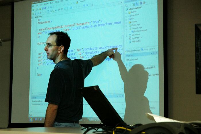 Teacher pointing at projected screen with code, demonstrating unhinged but effective teaching methods in the classroom.